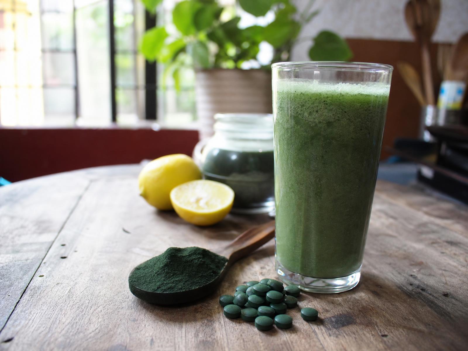 Spirulina powder in a rustic bowl surrounded by fresh green leaves